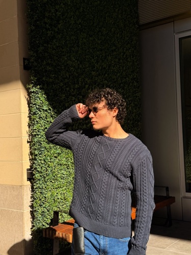 Alex in a cable-knit sweater against a green wall
